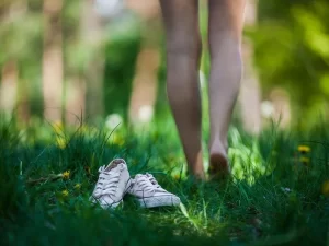 au 1er plan des chaussures, au 2ème plan une femme marchant pieds nus dans l'herbe