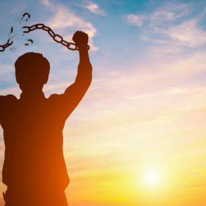 silhouette d'un homme brisant ses chaines sous un fond de coucher de soleil
