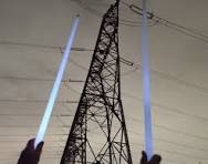 photo d'une ligne à haute tension et de 2 bras pointés vers elle tenant des néons qui s'allument